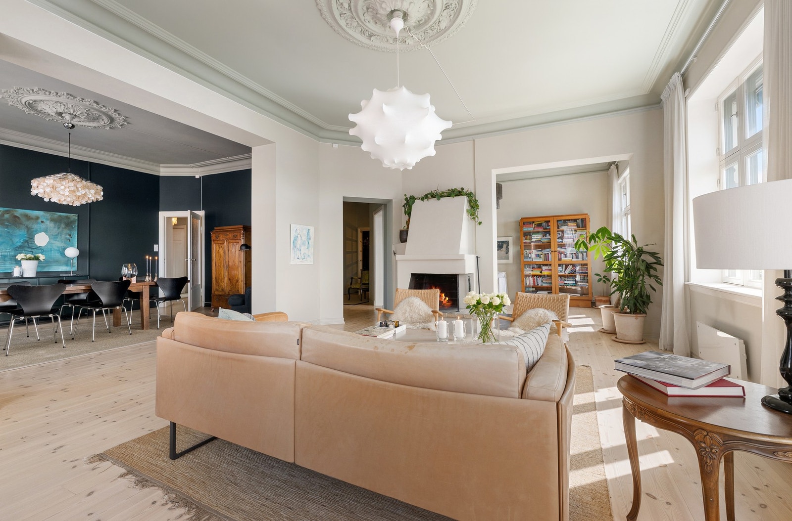 Stor stue med peis, stukkatur og naturlig sonedeling mot spisestue. Galleribilde
