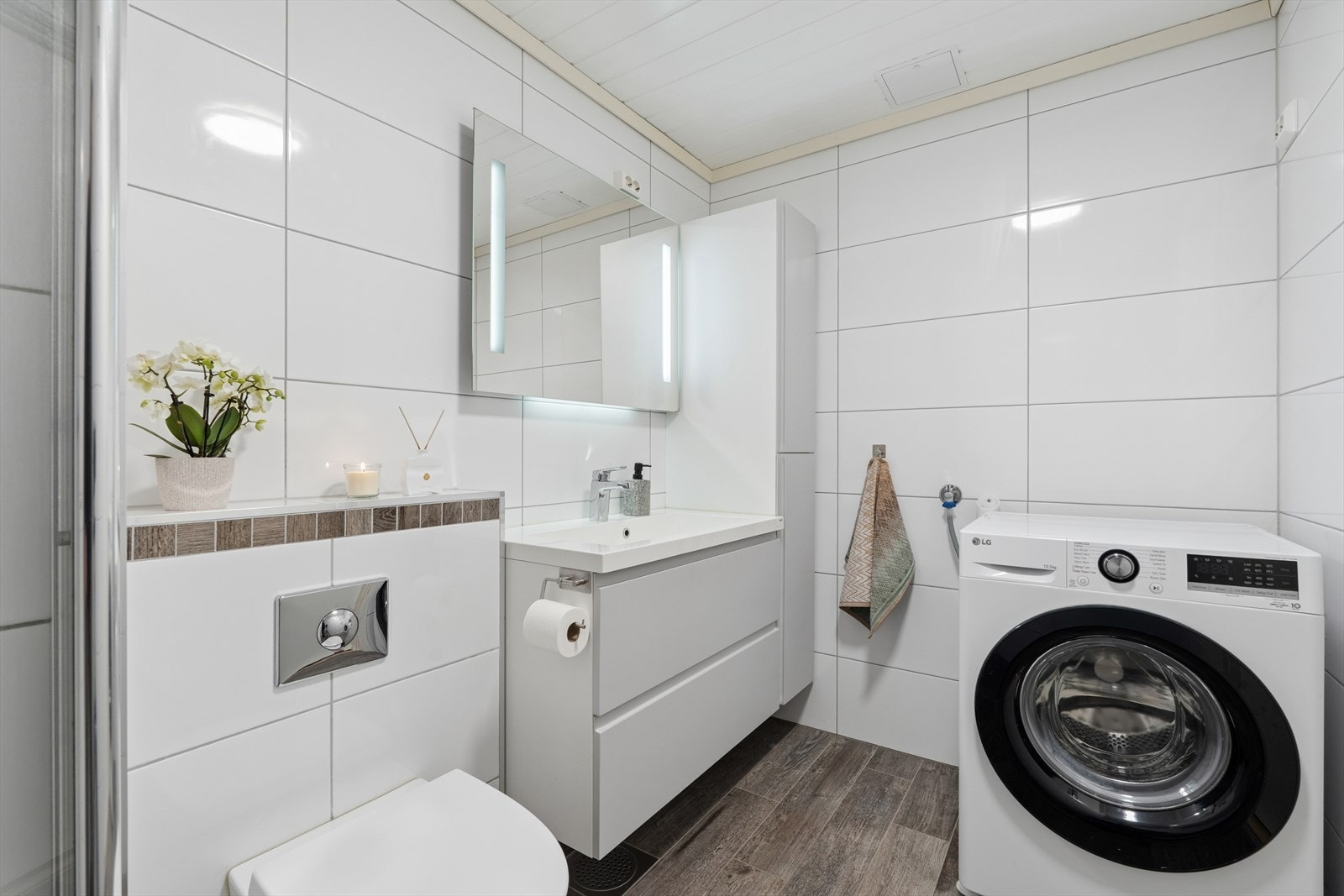På badet er det dusjnisje, vegghengt toalett, baderomsinnerdning og medfølgende vaskemaskin Galleribilde