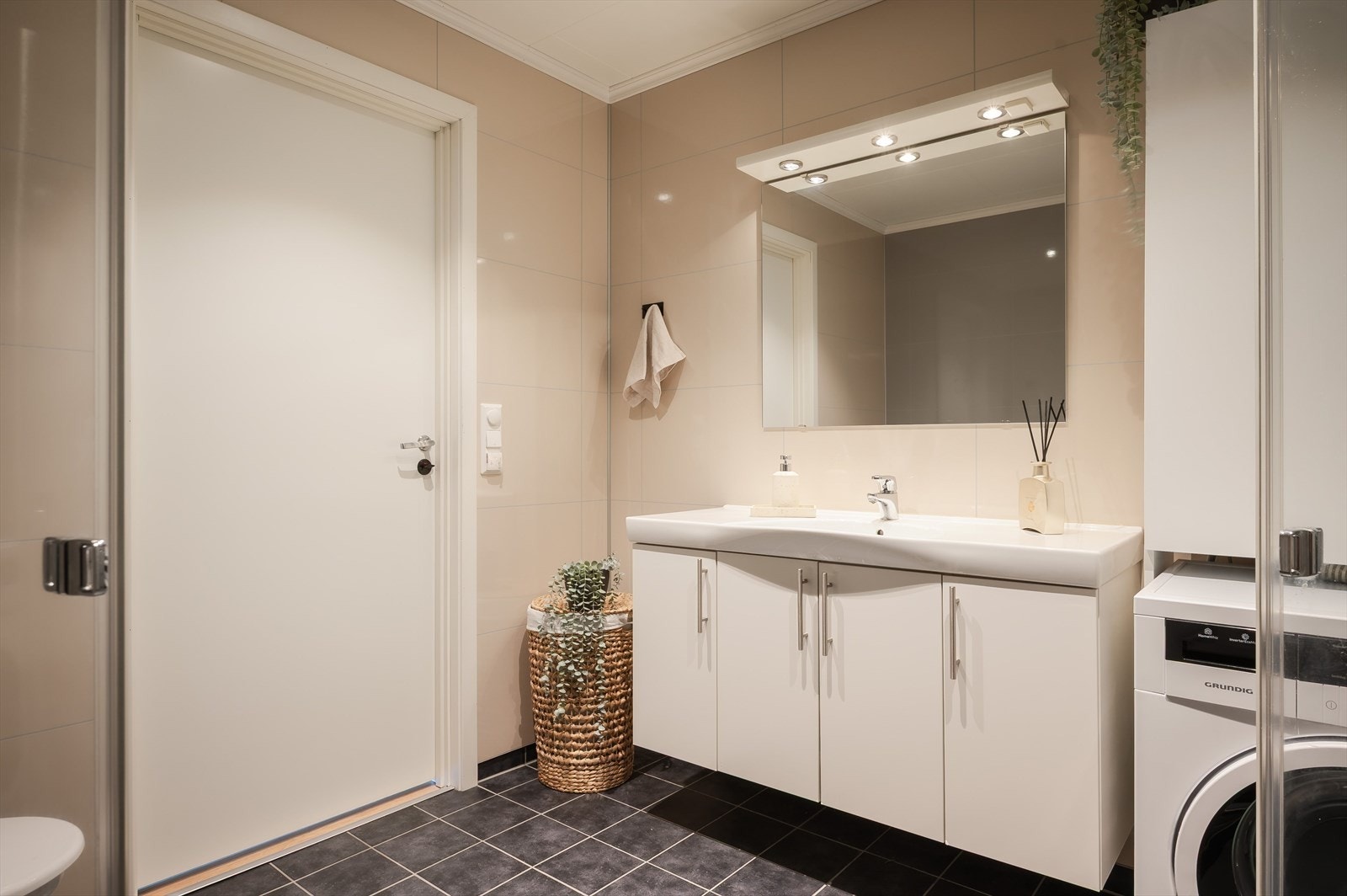 Leiligheten har et moderne baderom fra byggeåret 2014. Lys baderomsinnredning med heldekkende servant, stort speil med belysning over. I hjørnet er det plass og opplegg for vaskemaskin. Galleribilde
