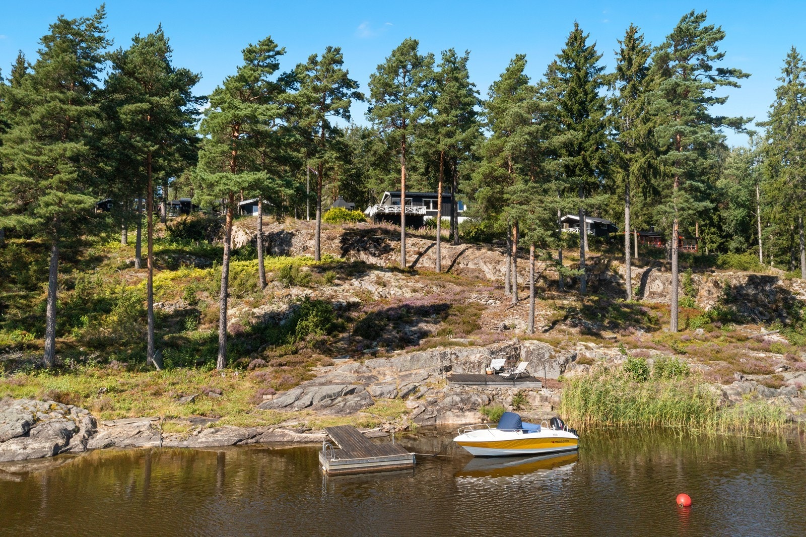 Hytta sett fra vannet, tilbaketrukket og privat i terrenget. Galleribilde