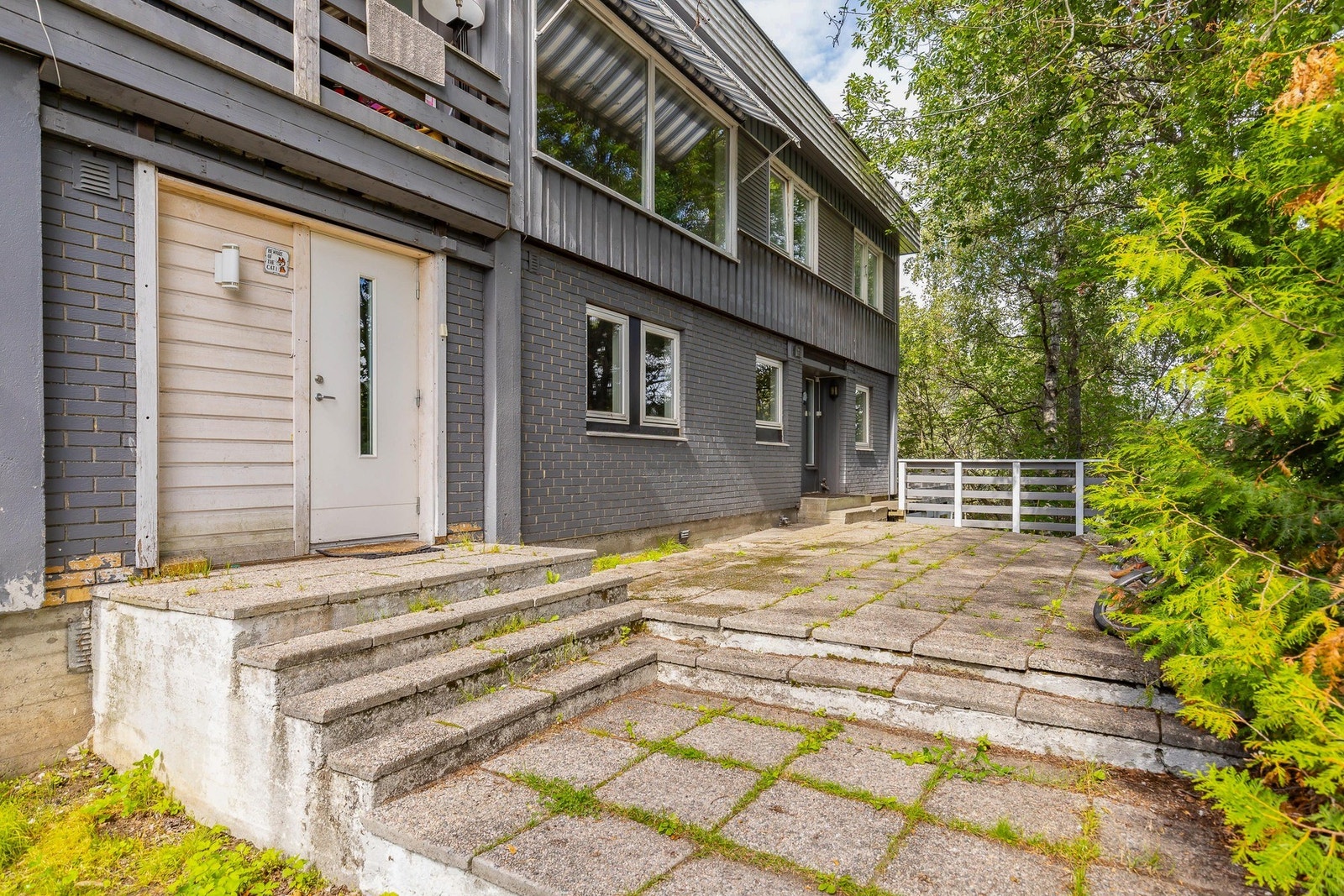En av boligens inngangspartier med grå murvegg, hvit dør og vindu, samt en liten trapp Galleribilde