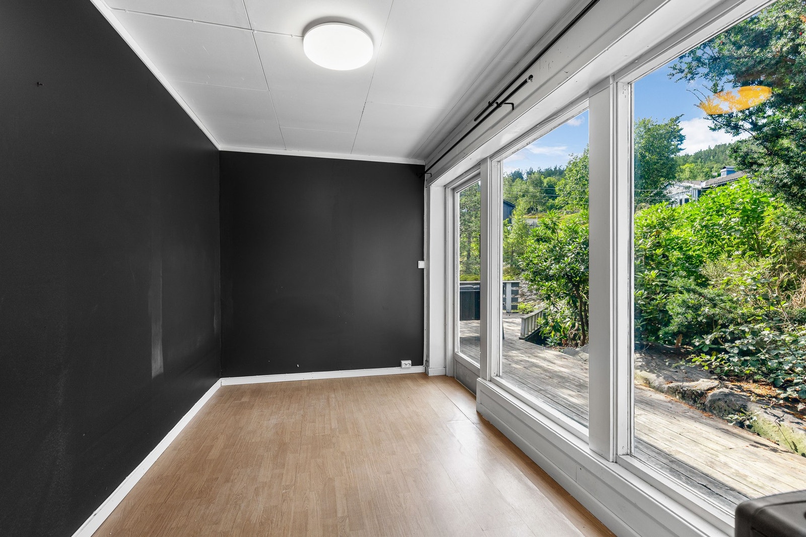 Rom med store vinduer som gir mye naturlig lys, samt utsikt mot hagen og skogkledde åser. Galleribilde