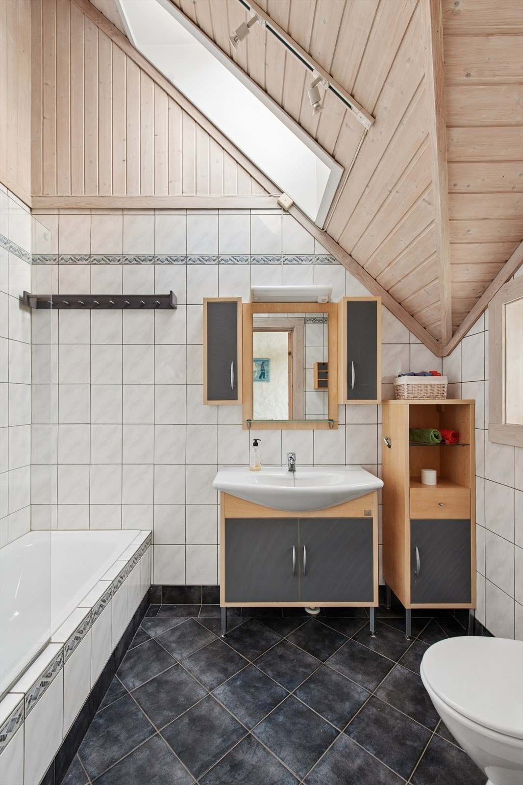 Hovedbadet er flislagt med gulvvarme og bestående av badekar, servant og toalett. Også her finner vi de arkitektoniske linjene i taket. Galleribilde