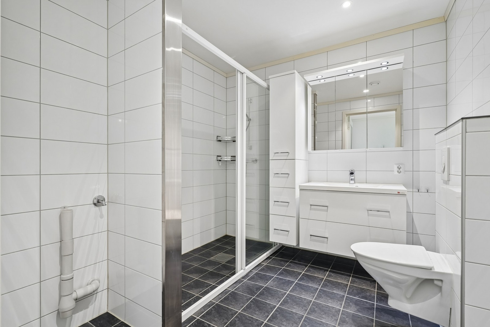 Badet kombineres med vaskerom og har opplegg , samt avsatt plass til vaskemaskin. Ellers har man vegghengt toalett og et stort baderomsmøbel med god skuffeplass og overliggende speilskap med belysning. Galleribilde
