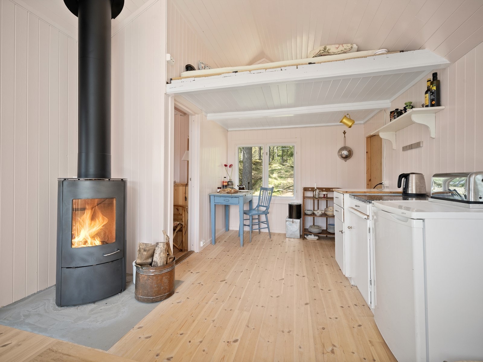 Stuen og kjøkkenet er et lunt allrom. En ny, isolert stålpipe og vedovn fra 2024 sørger for varme og hygge. Galleribilde