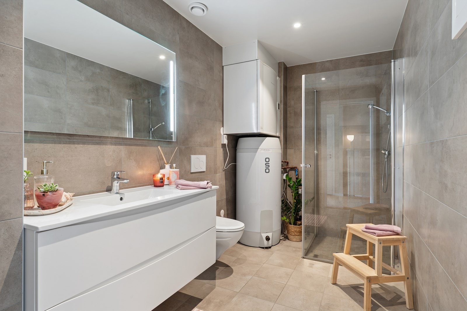 Sanitærutstyret består av moderne baderomsinnredning med nedfelt servant, veggmontert toalett og dusjvegger i hjørneløsning. Innredningen byr på gode oppbevaringsmuligheter, og speil med integrert belysning bidrar til et stilrent og funksjonelt preg Galleribilde