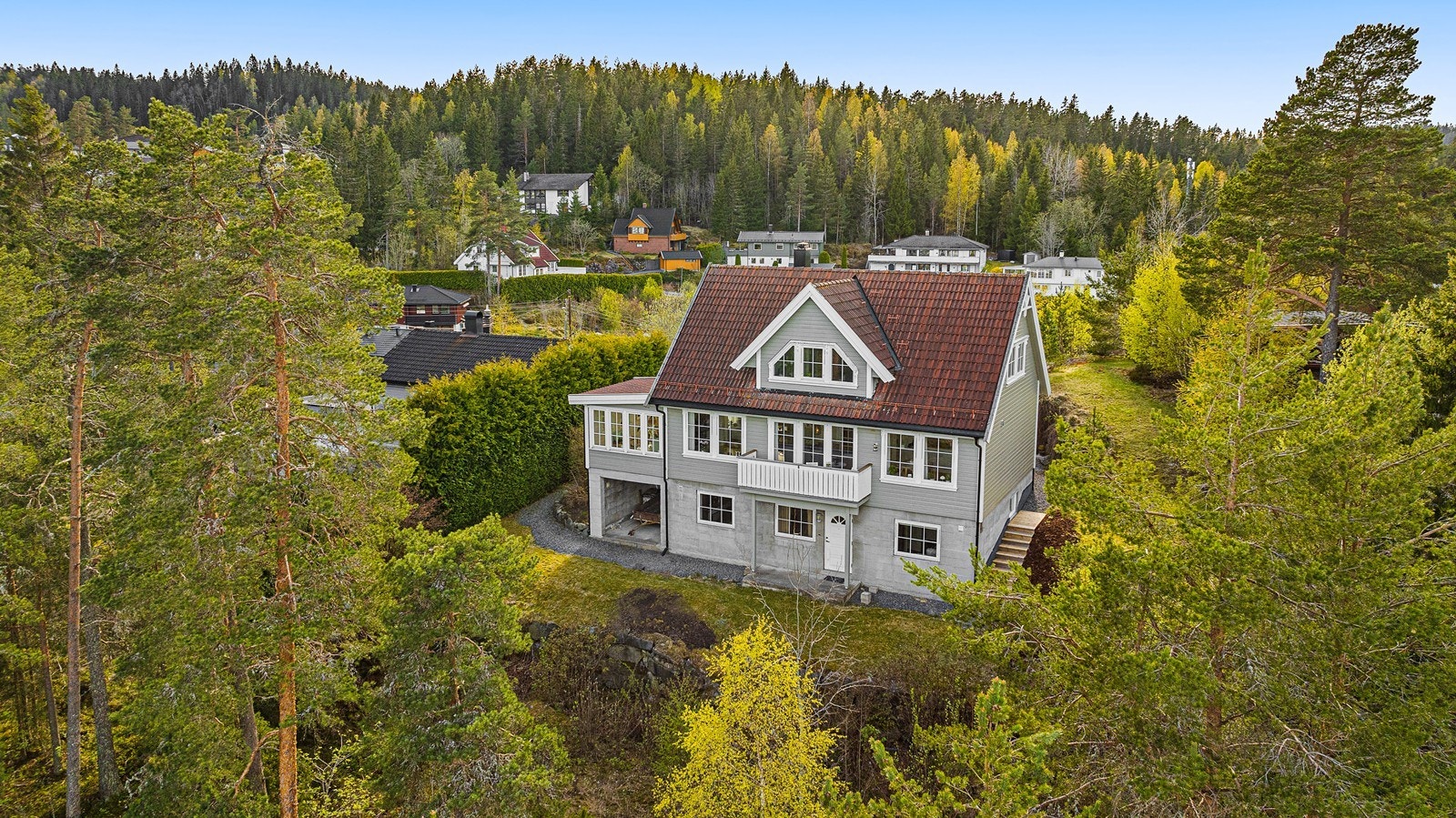 Tomten er pent opparbeidet med gress og beplantning, og terrenget har fall bort fra bygningen. Galleribilde