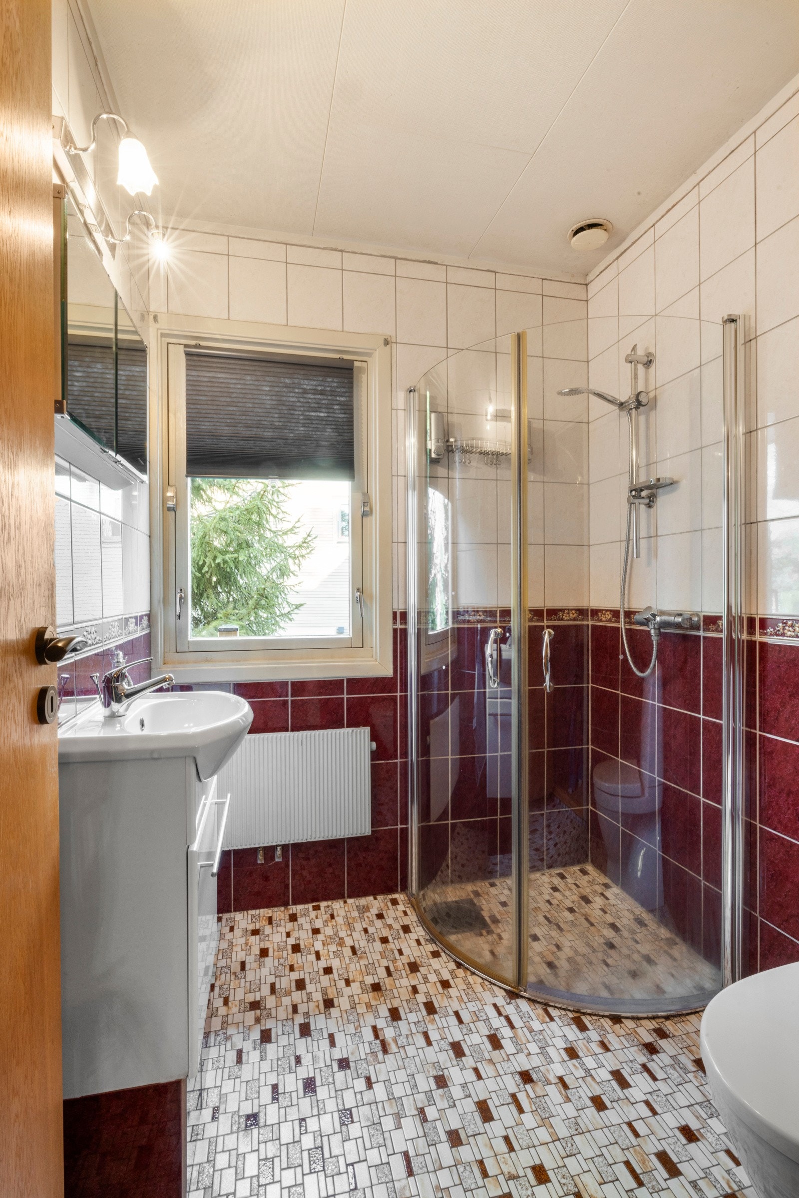 Badet ved gangen er innredet med frittstående toalett, dusjhjørne og hvit baderomsinnredning Galleribilde