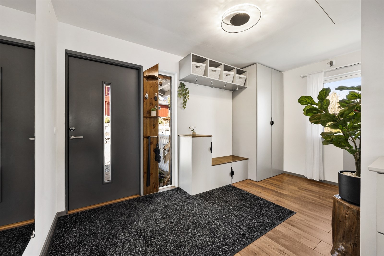Boligen har en bred entré med 1-stavs laminatgulv og hvitmalte veggflater. I entreen står det et lysegrått garderobeskap med tilhørende sittebenk ( skap og benk medfølger ikke ). Galleribilde