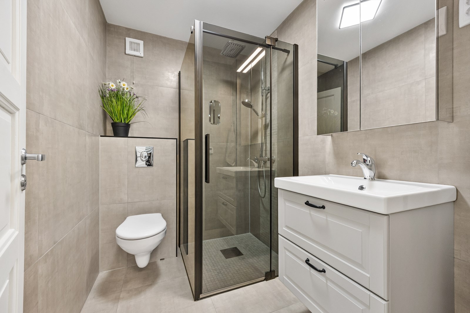 Badet i underetasjen er innredet med store, lysegrå vegg- og gulvfliser. På badet er det vegghengt toalett og vannbåren gulvvarme, og et dusjhjørne er utstyrt med regnfallsdusj. Galleribilde