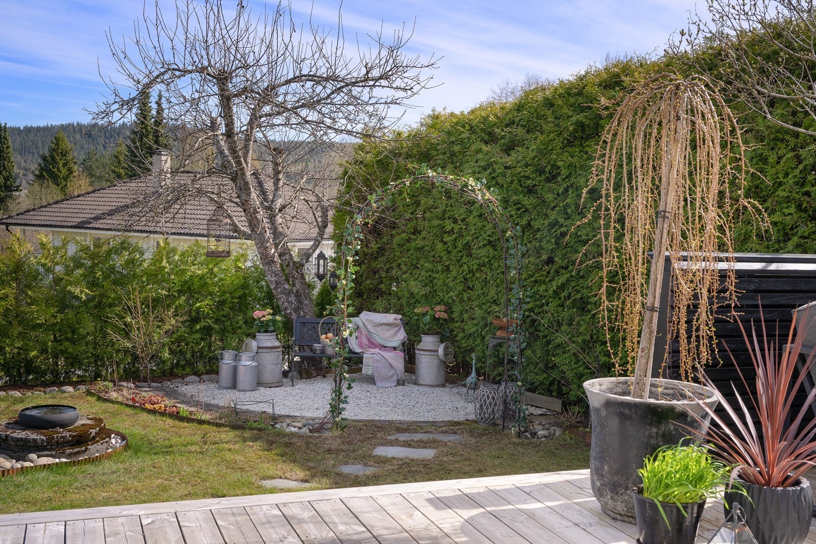 Hagen har flere sjarmerende sitteplasser, som denne usjenerte kroken. Denne hagekroken er inspirert av fransk hagestil, med variert beplantning, hvit elvesingel, hagebue med klatreplanter og dekorstein Galleribilde