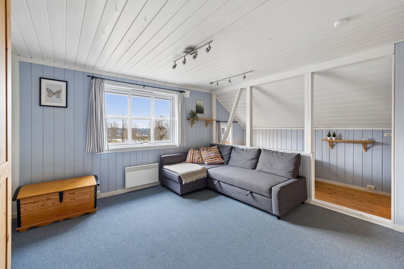 Soverom/loftsstue med vegg-til-vegg-teppe og malte panelflater i behagelige farger. Knekott er tatt inn i arealet. Galleribilde