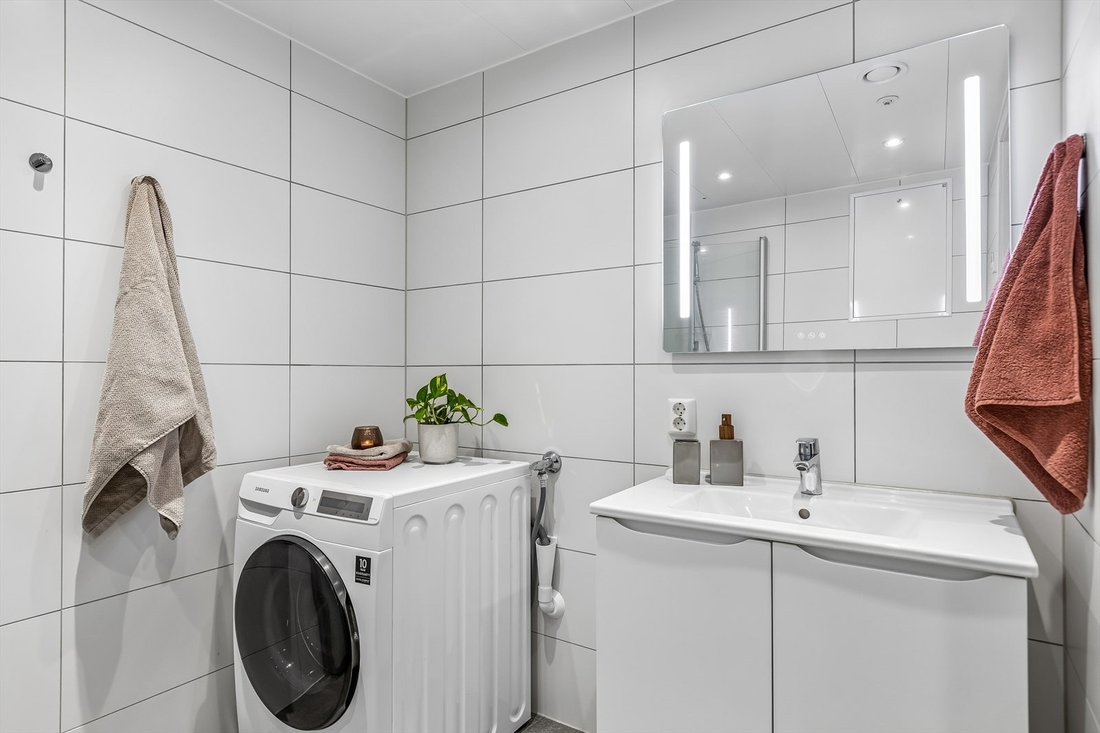Badet er utstyrt med dusjhjørne med dører, vegghengt toalett og opplegg for vaskemaskin. Galleribilde