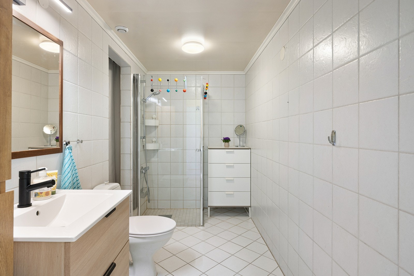 Badet er flislagt og fremstår som praktisk innredet med dusjløsning, servant med oppbevaring og opplegg for vaskemaskin. Galleribilde