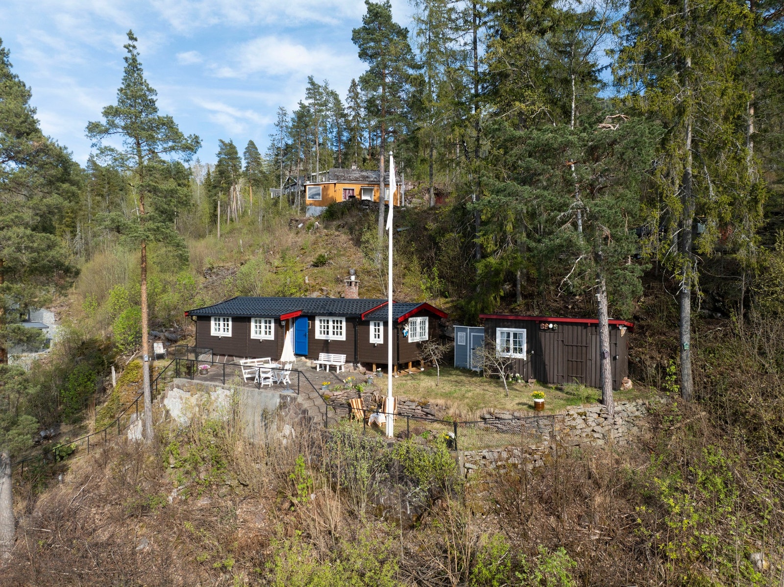 Hytta ligger på en fjellhylle og opparbeidet med steinmur og betong langs kanten. Galleribilde