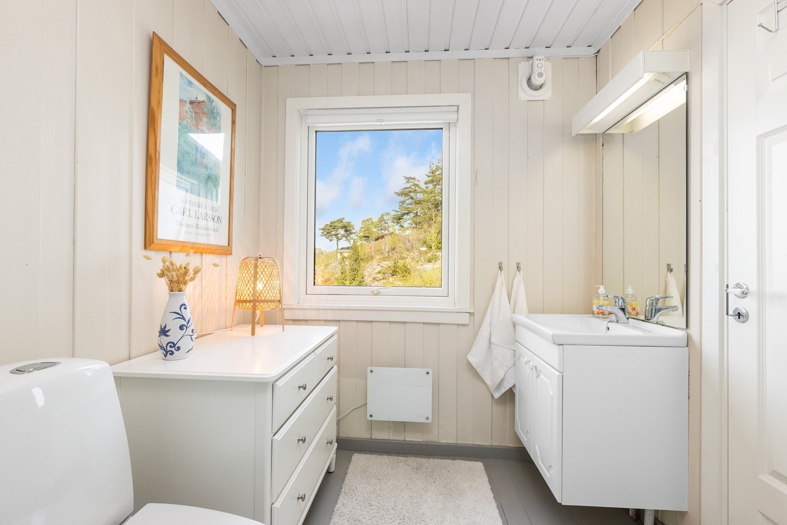 Lyst og pent bad med malte treoverflater. Badet er innredet med servantskap, servant, speil, dusjkabinett og toalett. Galleribilde