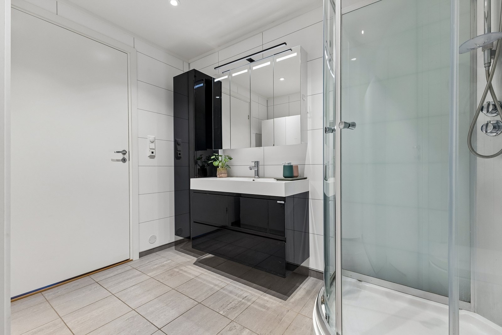 Badet fremstår moderne med flislagte overflater, vegghengt toalett, servantinnredning og dusjkabinett. Galleribilde
