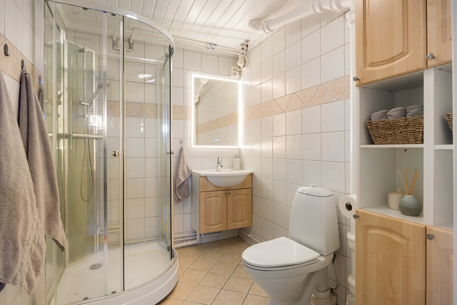 Badet i underetasjen har hvite veggfliser og beige gulvfliser. På badet er det toalett, dusjkabinett og varmekabler. Galleribilde