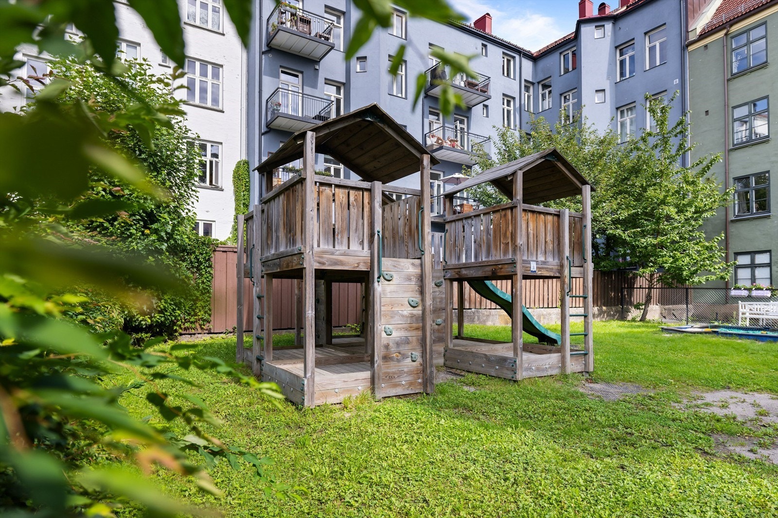 Lekeplass og bakgård med gressplen og sittebenker. Tomten er fellesareal. Galleribilde