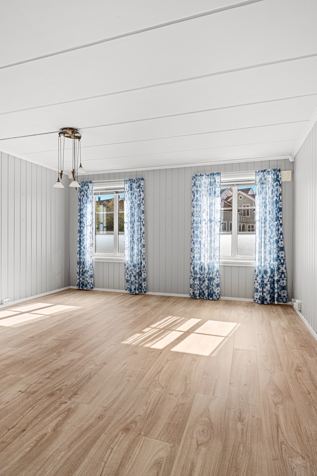 Romslig stue med lysmalte panelplater på veggene og nyere laminat på gulvet. Galleribilde