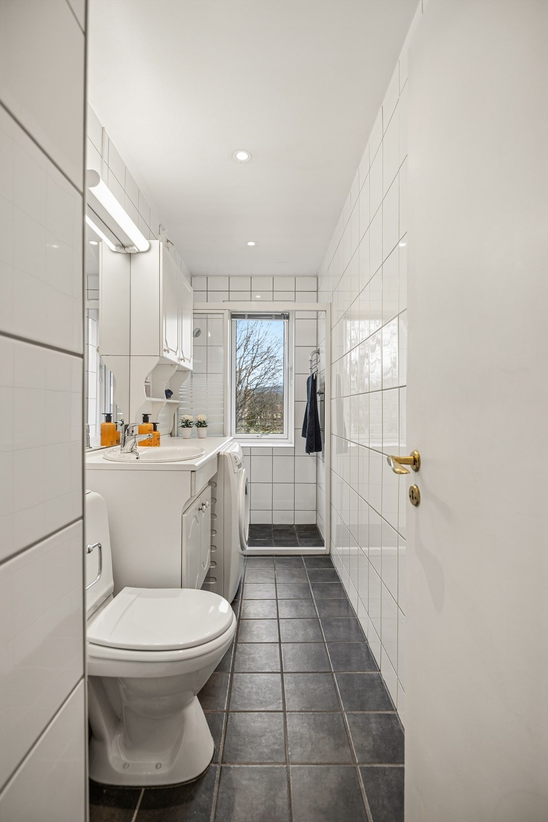 Flislagt bad med praktisk planløsning, dusjhjørne og vindu for naturlig ventilasjon. Badet fremstår som funksjonelt og normalt vedlikeholdt. Galleribilde