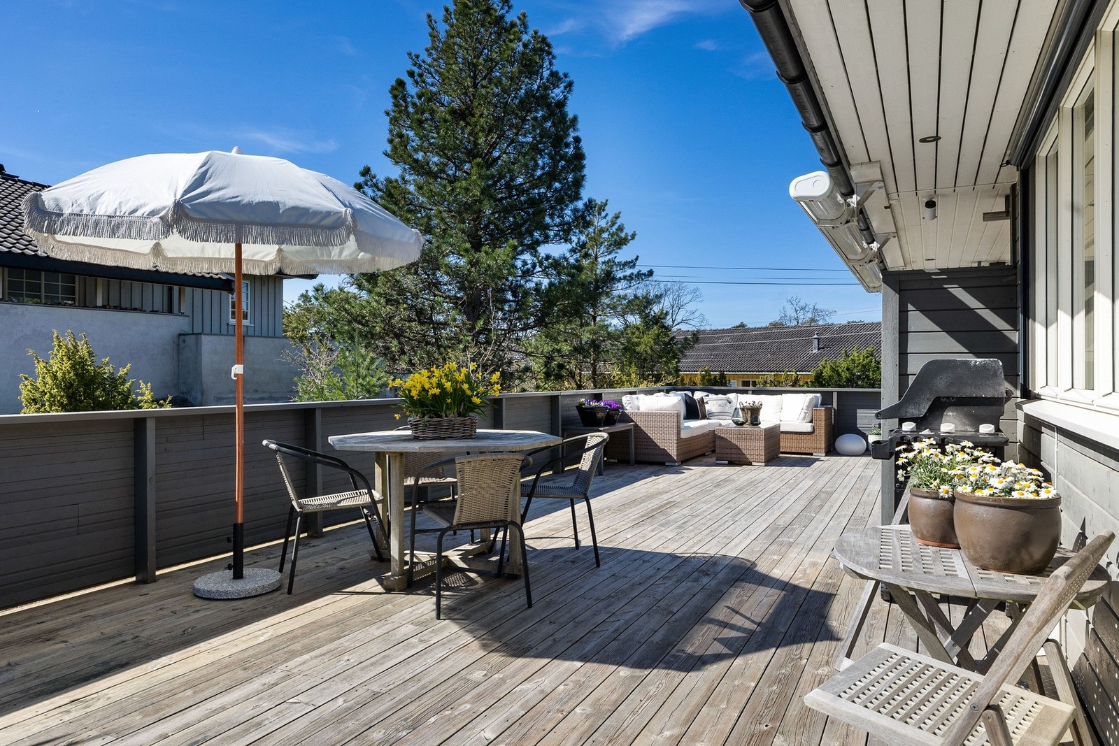 Stor terrasse med plass til utemøbler og grill, omgitt av frodig vegetasjon. Galleribilde