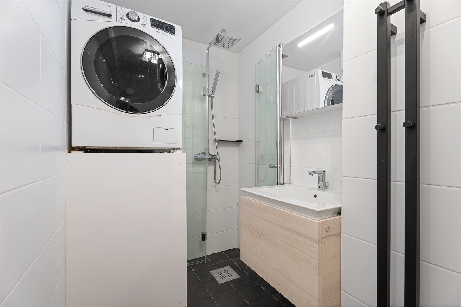 Badet er flislagt og har dusjnisje med innfellbare dører, regndusj, servant med skuffer samt overskap med lagringsplass. Det er også plass til vaskemaskin og varmtvannsberederen er plassbygd. Galleribilde