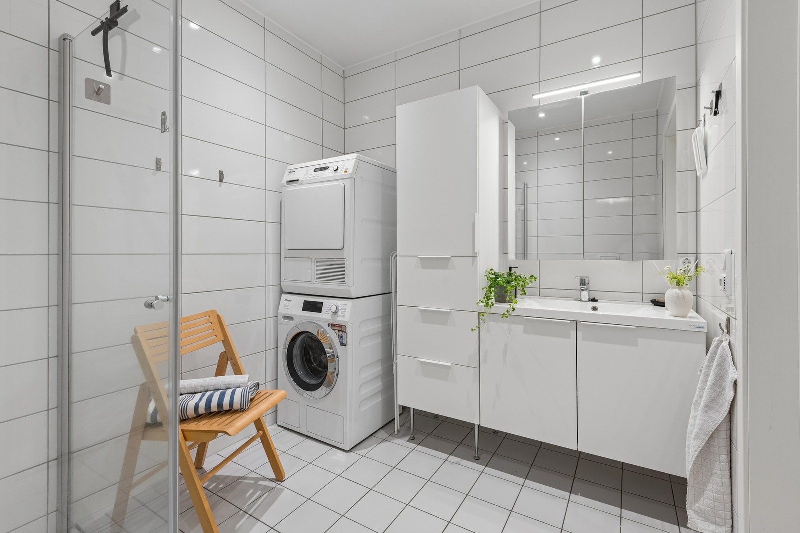 Badet har åpen dusjløsning med glassdører, god oppbevaringsplass i innredning og opplegg for vaskemaskin og tørketrommel. Galleribilde