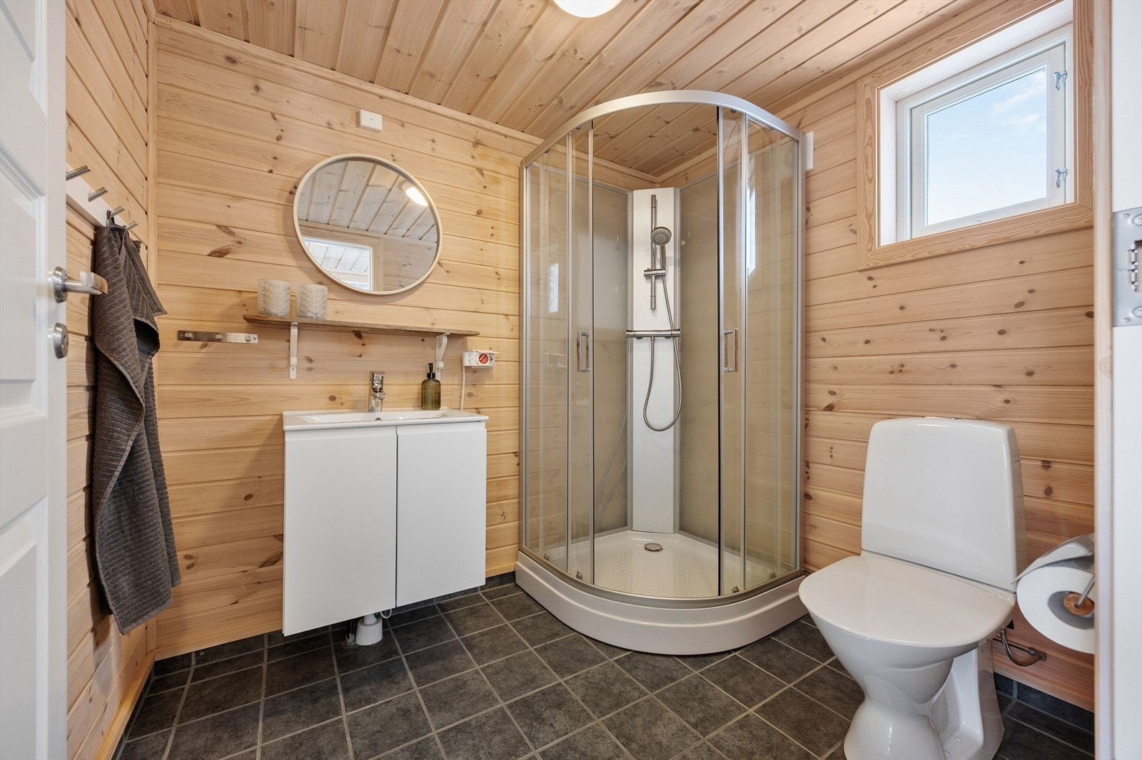 Badet fremstår som pent, velholdt og praktisk, og har naturlig panel på veggene og koksgrå fliser på gulv med gulvvarme. Galleribilde