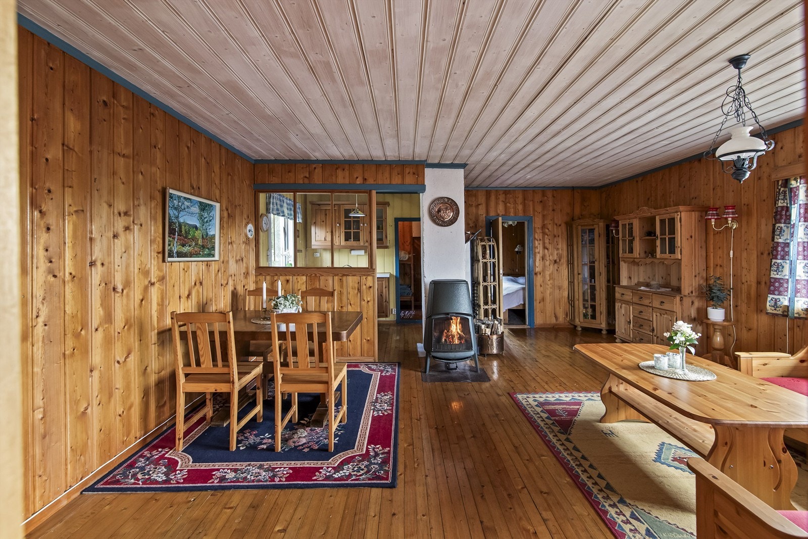 Stuen er hyttas samlingspunkt, med klassisk trepanel på vegger og i tak, furugulv og en sentralt plassert vedovn for varme og hygge. Galleribilde