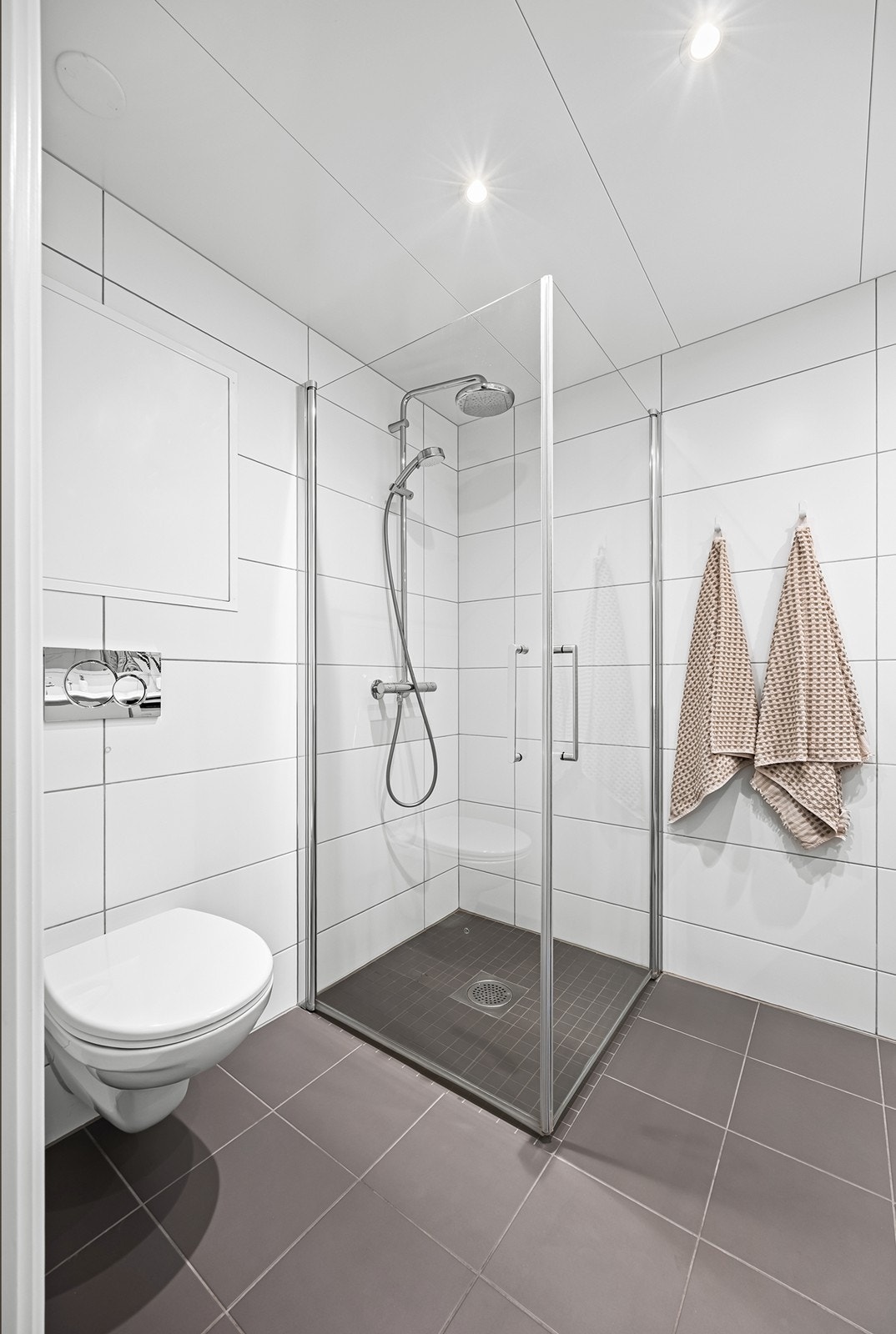 Badet er innredet med vegghengt toalett, servant nedfelt i innredning med ettgreps blandebatteri samt dusjhjørne med svingbare glassdører. Galleribilde