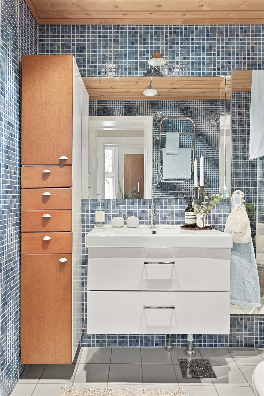 Overflatene på vegger og gulv er flislagt, og himling er trepanel. Badet er innredet med en nedfelt servant, overhengende speil og belysning. Galleribilde