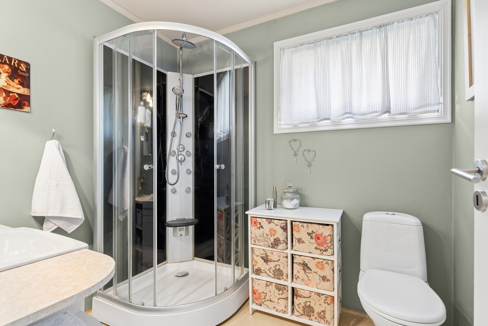 Badet har vinylbelegg på gulv og malte vegger. Badet er innredet med toalett, servantinnredning og dusjkabinett. Oppvarming skjer via panelovn. Galleribilde