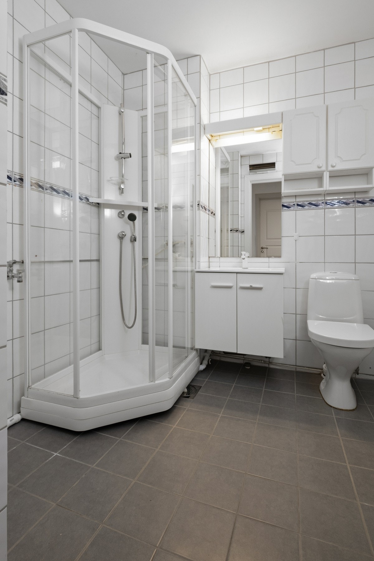 Badet fremstår som praktisk og fint, med hvite fliser på veggene og grå fliser på gulv med sluk Galleribilde