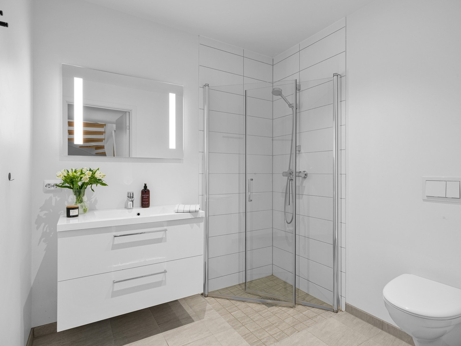 Badet har fliser på gulv med varmekabler, fliser på vegger i dusjsonene, samt malte overflater på vegger. Badet er innredet med servantskap og speil med belysning. Galleribilde