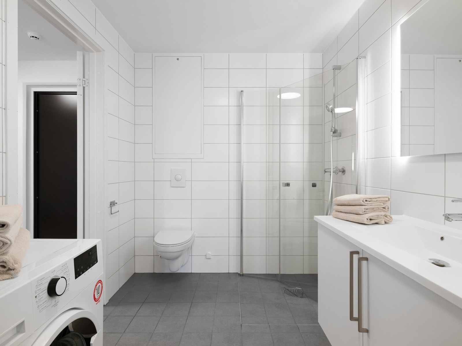 Badet er innredet med servantskap og speil med belysning. Videre er rommet utstyrt med toalett, dusj og opplegg til vaskemaskin. Galleribilde