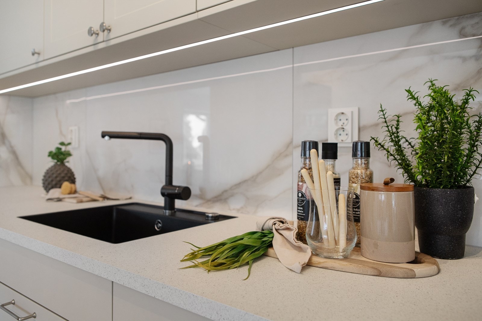 Appstyrt lys over kjøkkenbenk, samt bevegelsessensor under overskap for slå av/på og dimme opp eller ned. Fliser 60X120 mellom kjøkkenbenk og overskap. Det er montert komfyrvakt og sensorer for vannstopper i kjøkkenbenk og under oppvaskmaskin Galleribilde