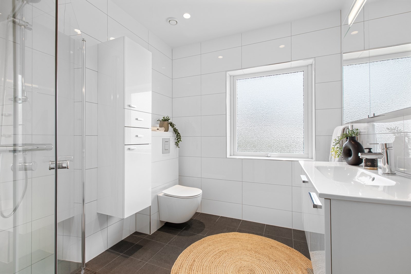 Badet i første etasje er flislagt og har elektriske varmekabler i gulvet. Nytt vegghengt toalett fra 2026. Nytt tak (malte gipsplater med Aqua maling) med spotter fra 2026. Ny termostat og brytere fra 2026. Galleribilde