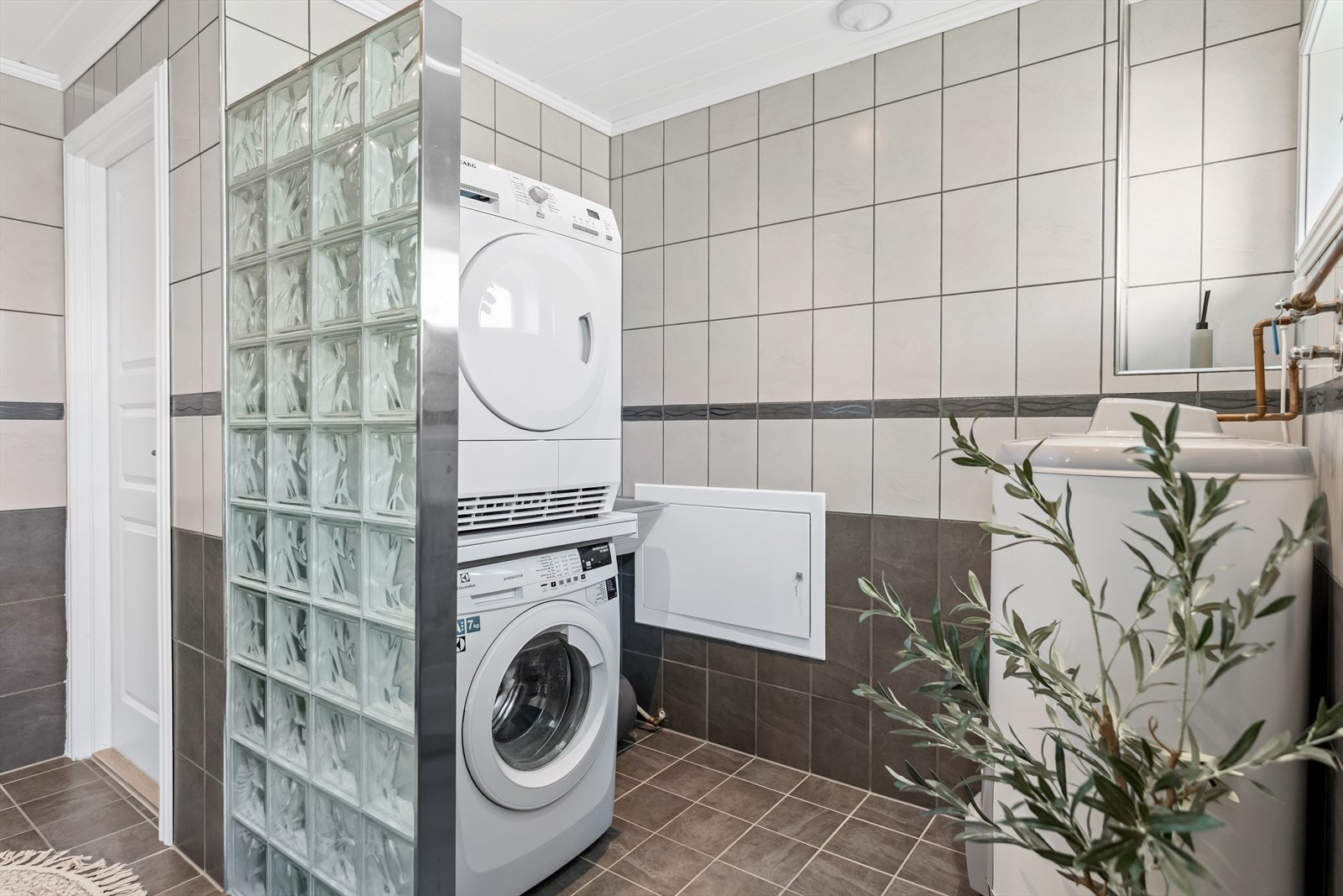 Varme er lagt i gulvet, og badet har downlights, vegghengt toalett og opplegg for vaskemaskin bak en vegg av glassbyggerstein. Galleribilde