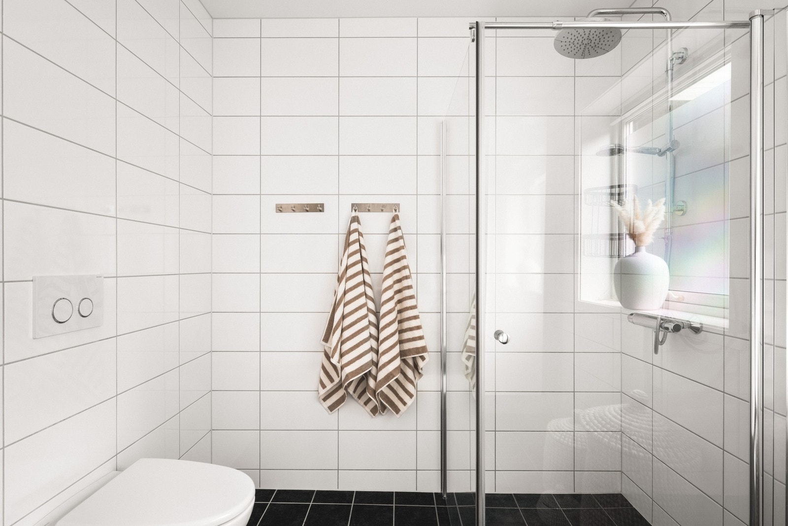 Badet inneholder vegghengt toalett, helstøpt servant, skuffer under servant med slette fronter og dusjdører i klart glass Galleribilde
