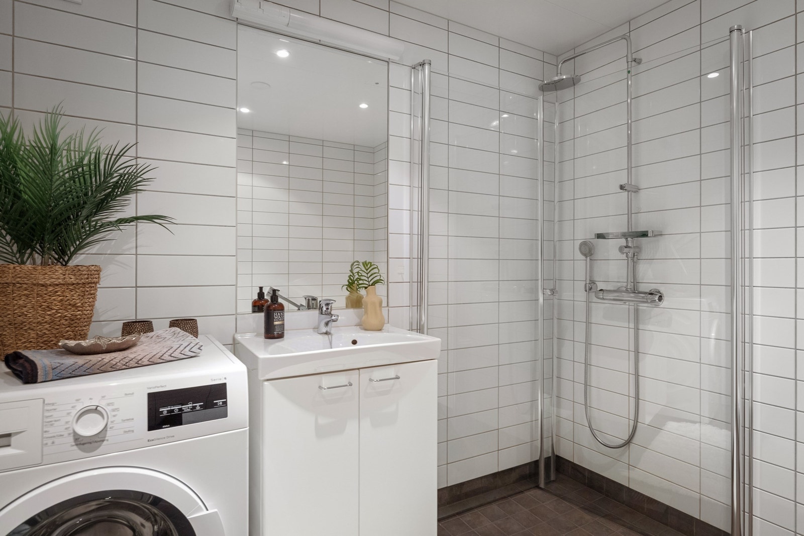 Badet er innredet med vegghengt klosett, servant nedfelt i innredning, speil med lys og dusjhjørne med svingbare, plassbesparende glassdører Galleribilde