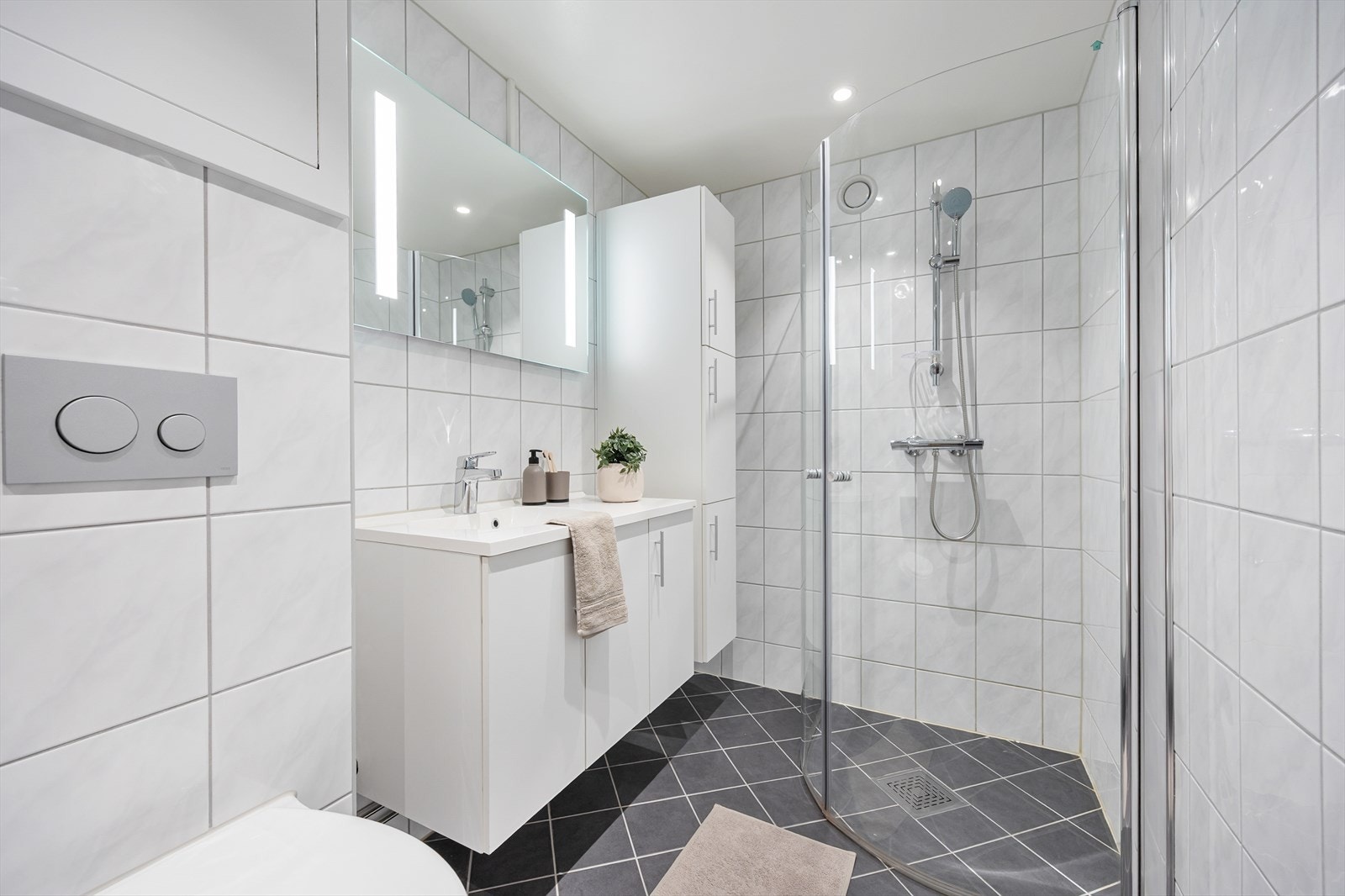 Badet er utstyrt med dusjhjørne, vegghengt toalett og servantinnredning med oppbevaring. Galleribilde