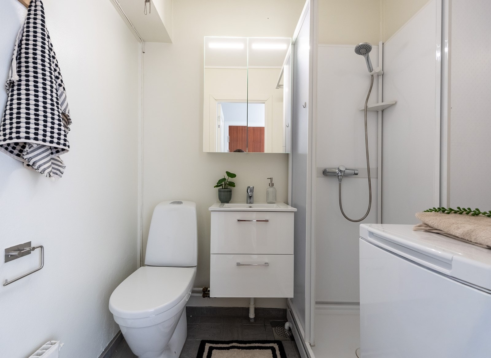 Lyst bad utstyrt med vaskemaskin, dusjkabinett, wc, servantskap, speilskap m/lys, radiator og stoppekran. Galleribilde