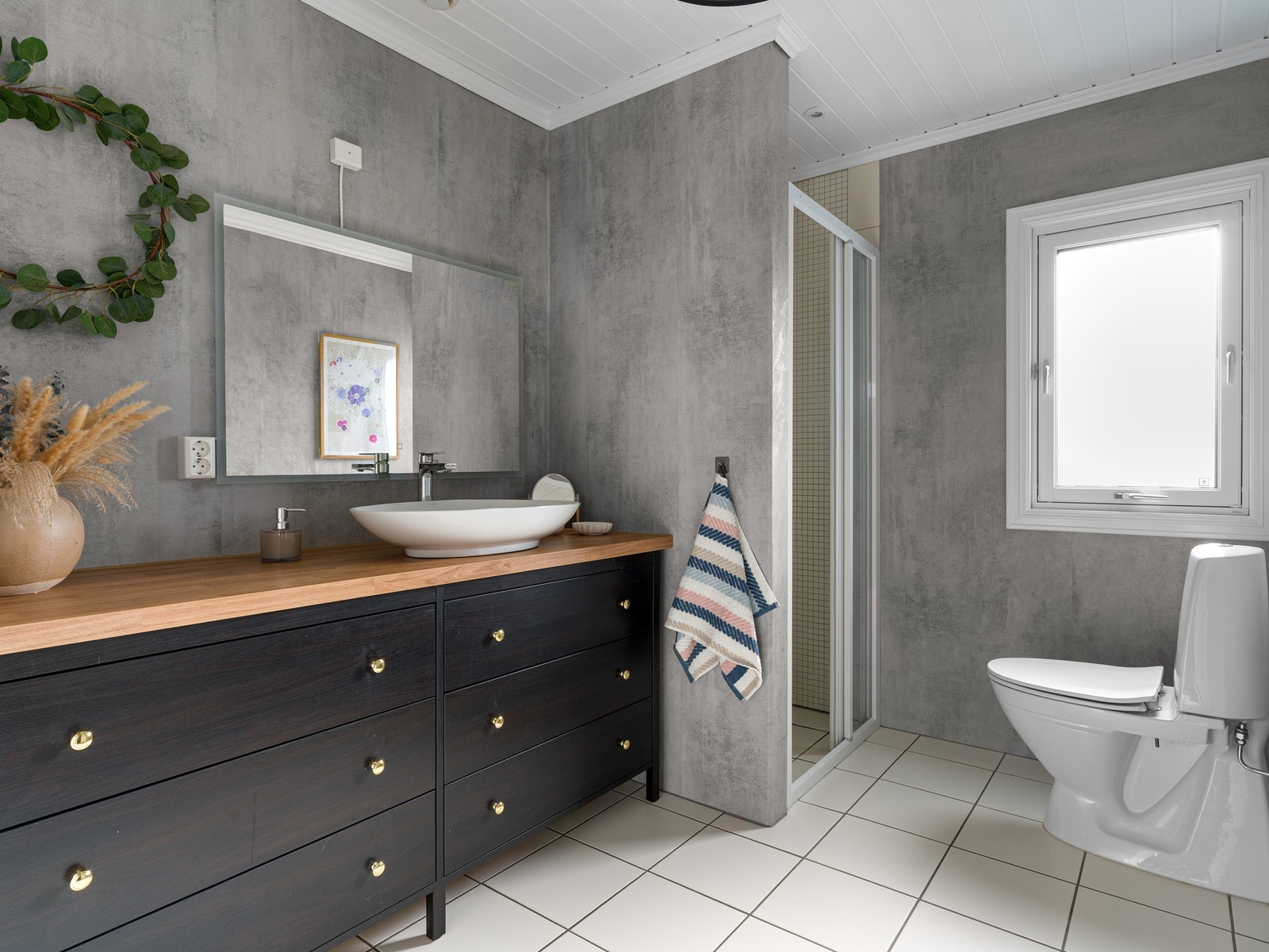 Badet i første etasje har fliser på gulv og fliser/tapet på vegger. Badet er innredet med servant på innredning og speil. Videre er rommet utstyrt med toalett og dusj. Galleribilde