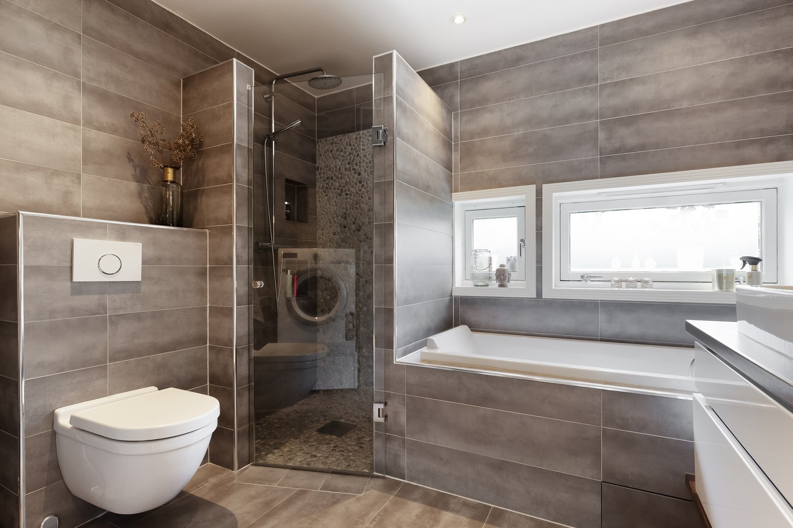Toalettet er vegghengt med innebygget sisterne. Det er opplegg for vaskemaskin. Videre har badet dusjhjørne med glassfelt og badekar. Galleribilde