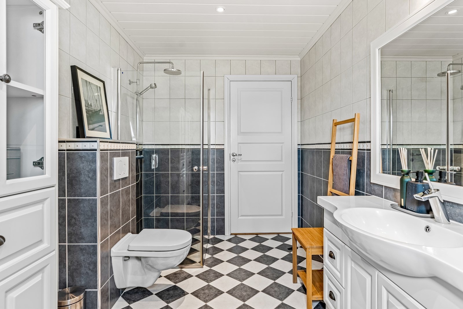 Badet i første etasje har frostet(folie) vindu, gulvvarme, hvitmalte panelplater med downlights og høyttalere i taket, samt grå og hvite fliser på gulv og vegger. Galleribilde