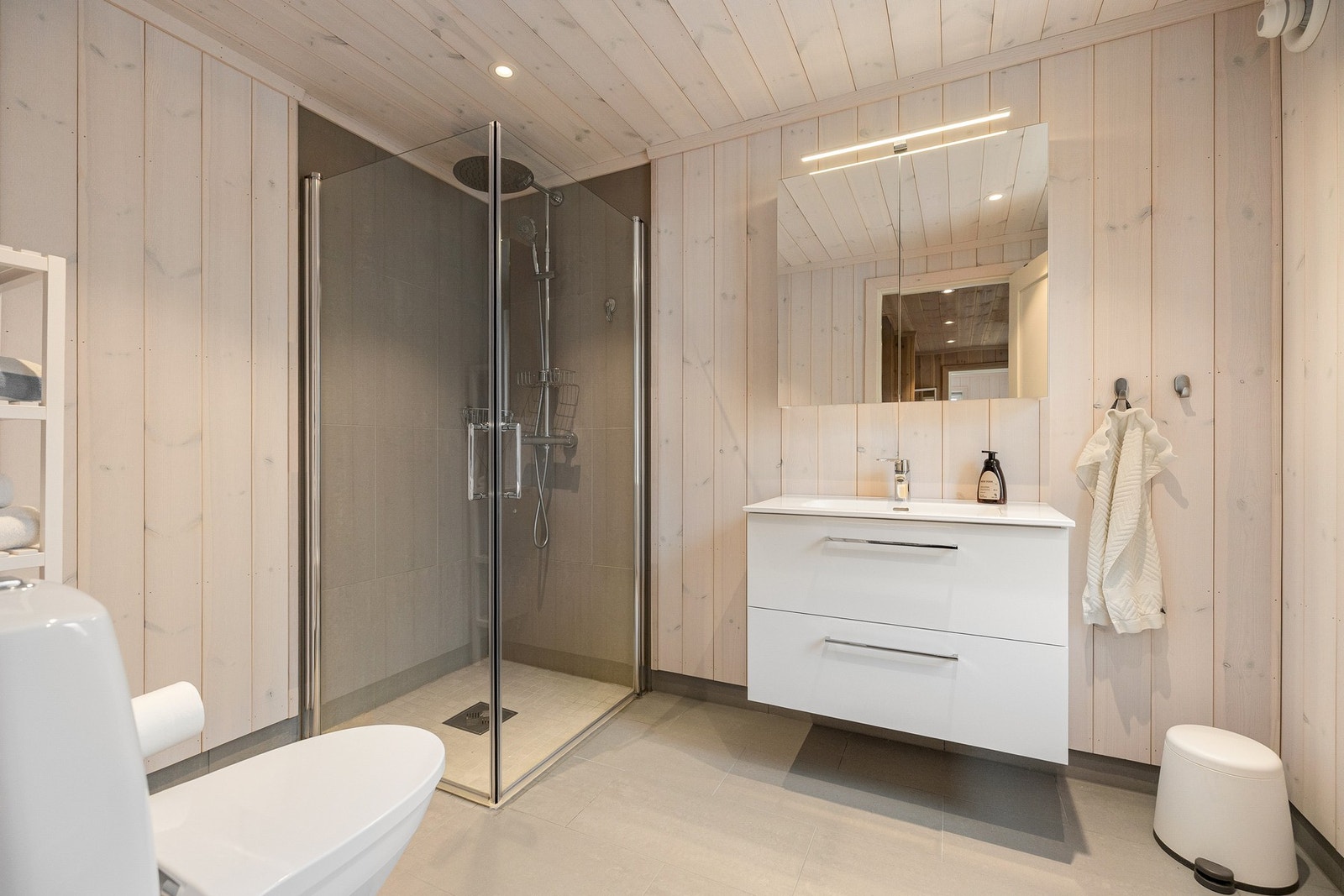 Badet er utført med flislagt gulv med elektriske varmekabler, kombinert med fliser og trepanel på vegger og panel i himling. Galleribilde
