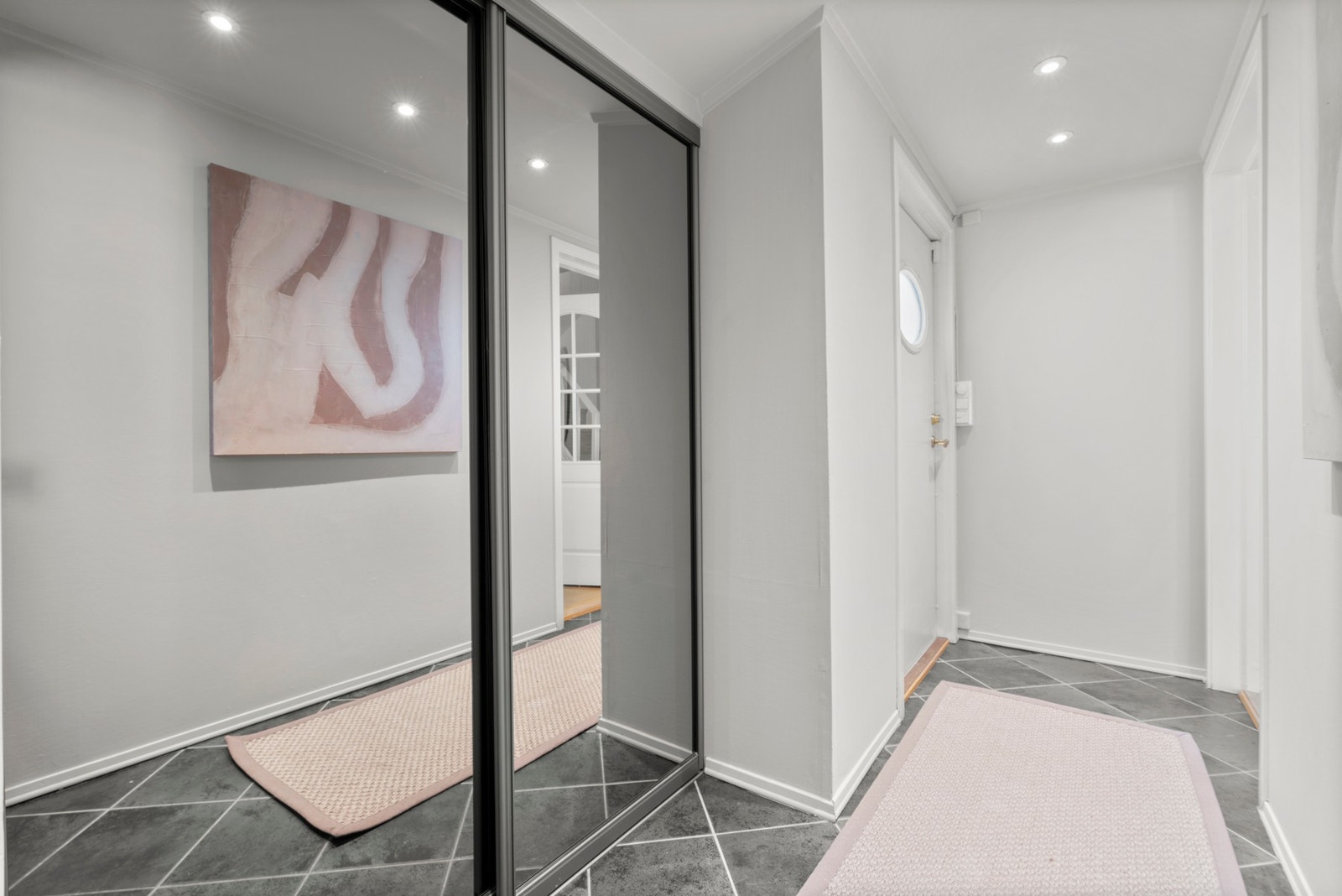 Vel inne har gangen downlights, varmekabler og mørke fliser på gulvet. Yttertøyet ryddes enkelt bort i en innebygd skyvedørsgarderobe med speilfronter. Galleribilde
