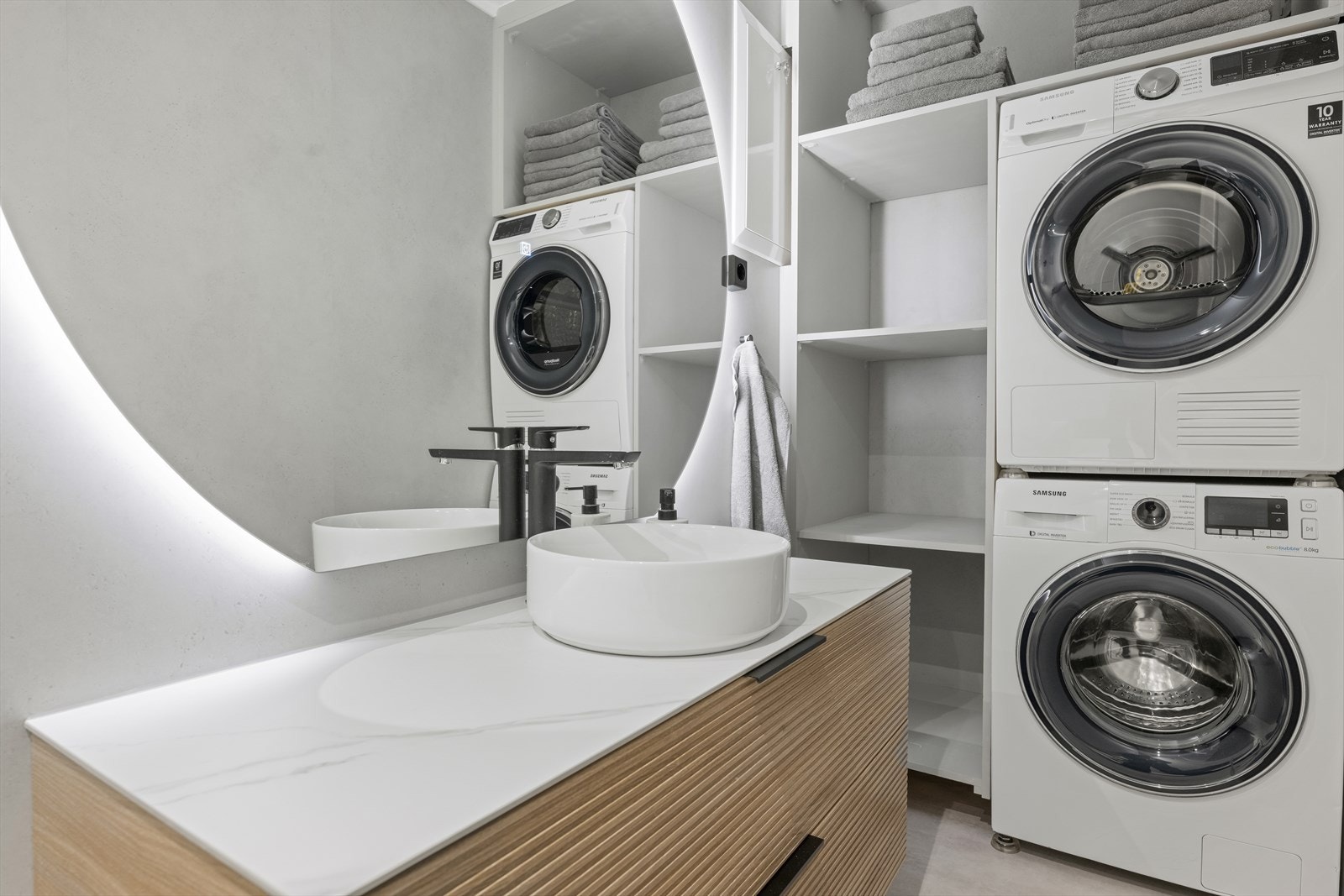 Innredningen er moderne med påstående servant over innredning, opplegg for vaskemaskin, dusjvegger i glass, dusjgarnityr på vegg og speil med integrert lys. Galleribilde