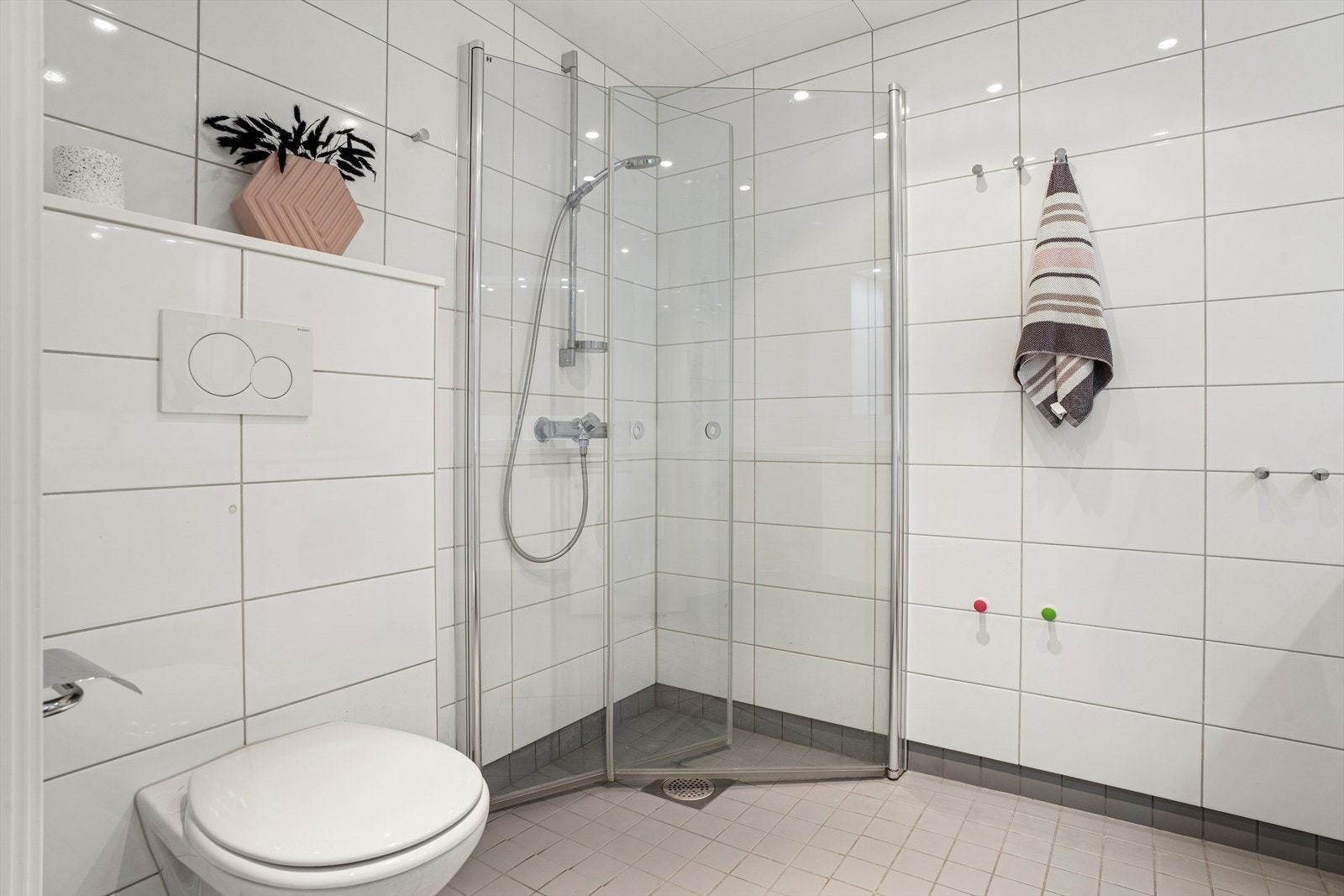Badet er utstyrt med vegghengt toalett, dusjhjørne med innfellbare dører, samt en baderomsinnredning med servant og overskap. Galleribilde